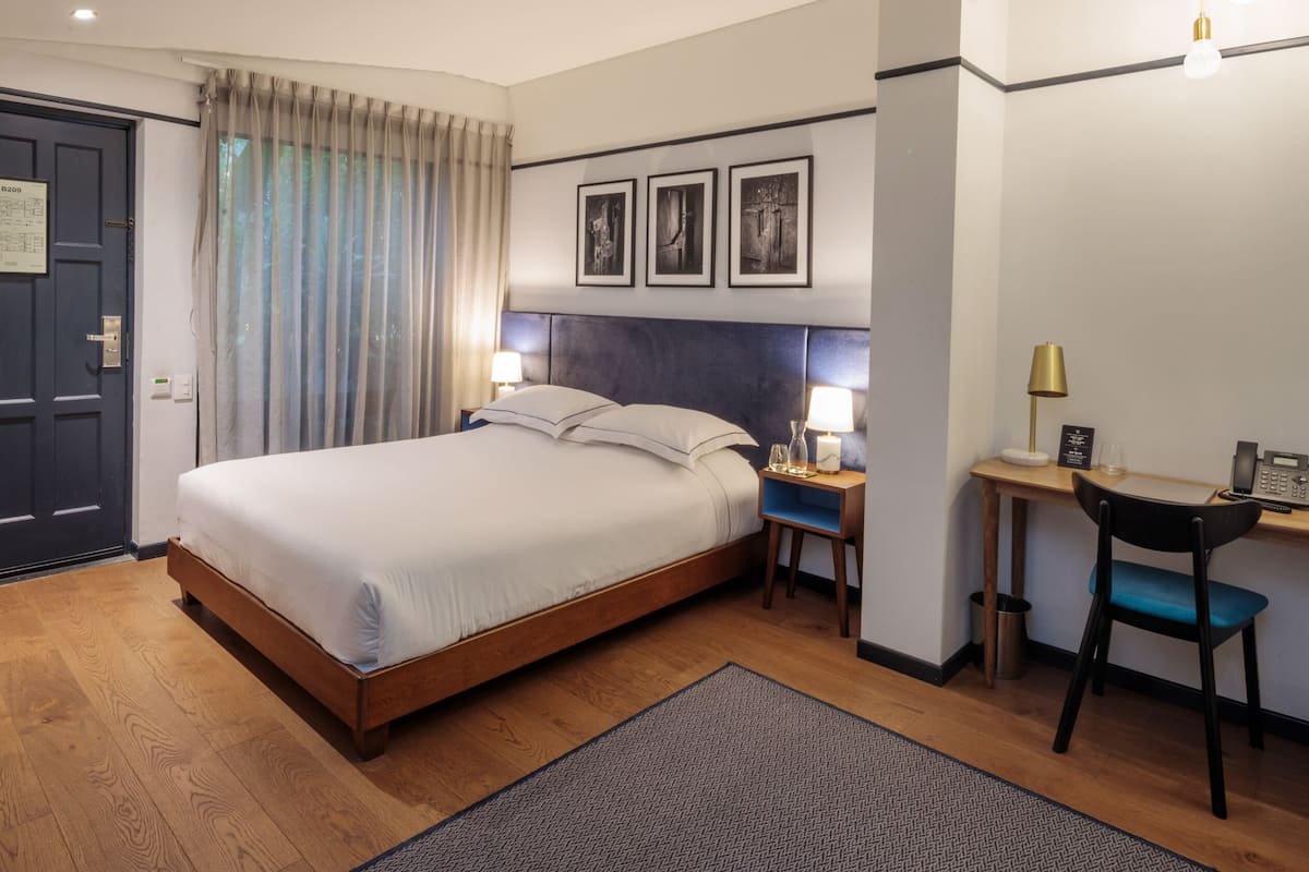 A hotel room with a bed, desk, chair, and a door with a sign.