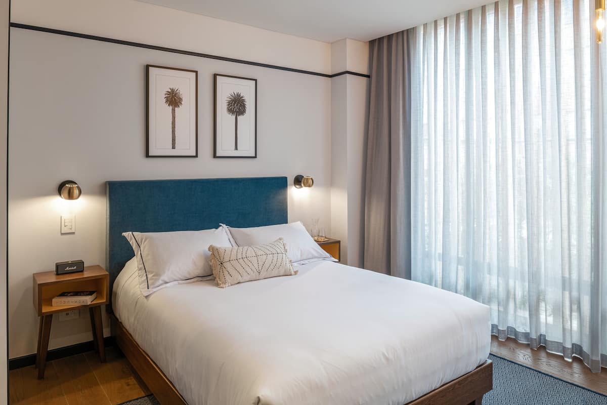A neatly made bed with white linens, a blue headboard, and two framed pictures on the wall.