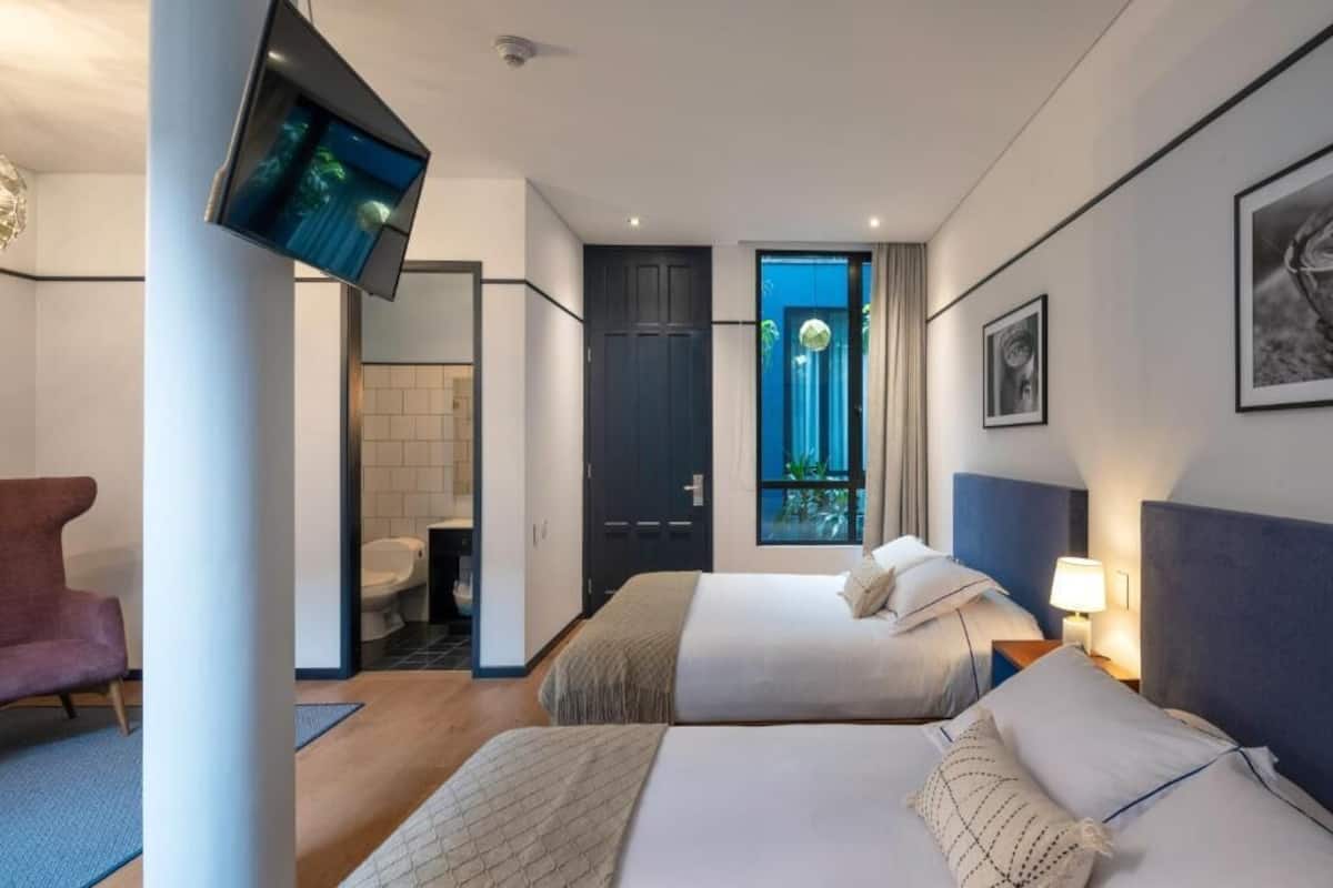 A hotel room with two beds, a TV, a chair, a bathroom, and a window with a view.