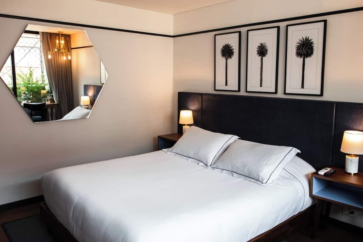 A hotel room with a bed, two bedside tables with lamps, a round mirror, and three framed pictures on the wall.