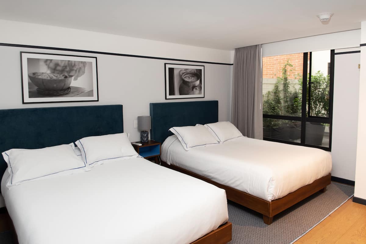 A hotel room with two single beds, a nightstand, a framed picture, and a large window with a view of the outside.