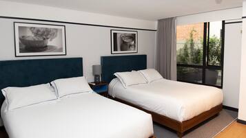 A hotel room with two single beds, a nightstand, a framed picture, and a large window with a view of the outside.