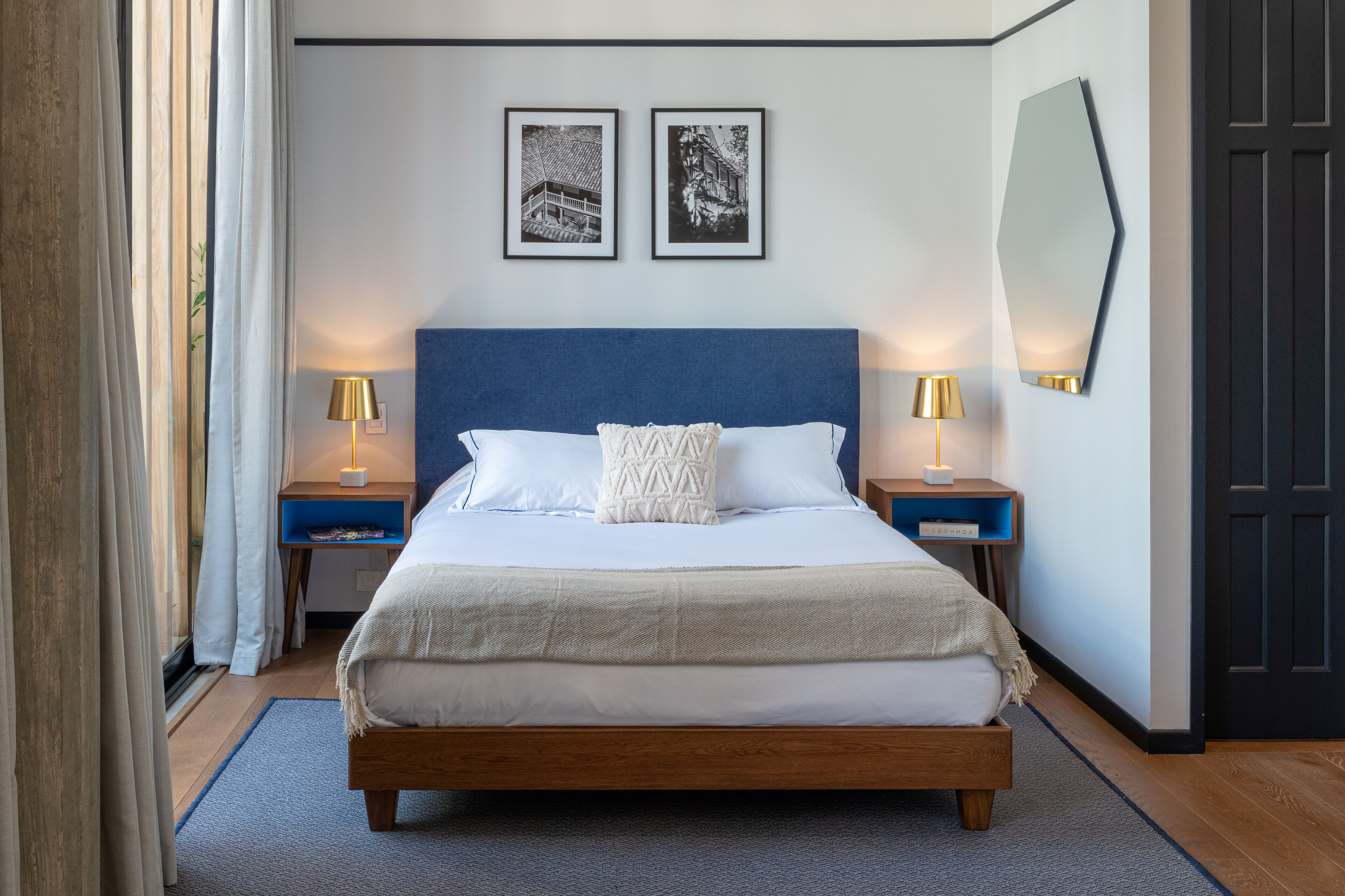Un dormitorio ordenado con una cama grande, dos mesitas de noche con lámparas y dos cuadros en la pared.