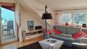 En stue med sofa, sofabord, lampe, tv-møbel og et vindue med gardiner.