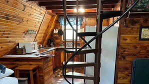 Interior acogedor de una cabaña con escalera espiral, paredes de madera, una zona de cocina y una cama.
