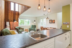 A modern kitchen with a granite countertop, stainless steel sink, and pendant lighting. - Winter Wren Mount Washignton Village (Courtenay)