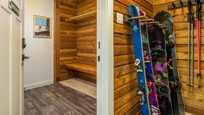A wooden interior with a bench, a wall-mounted ski rack, and a door leading to another room.