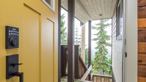 A wooden staircase leading to a balcony with a view of tall trees.