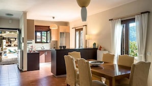 A spacious kitchen with a central island, dining area with chairs, and a view of a garden through large windows. - Luxurious Pool Villa Kavalos (6-11people) (Kavallos)