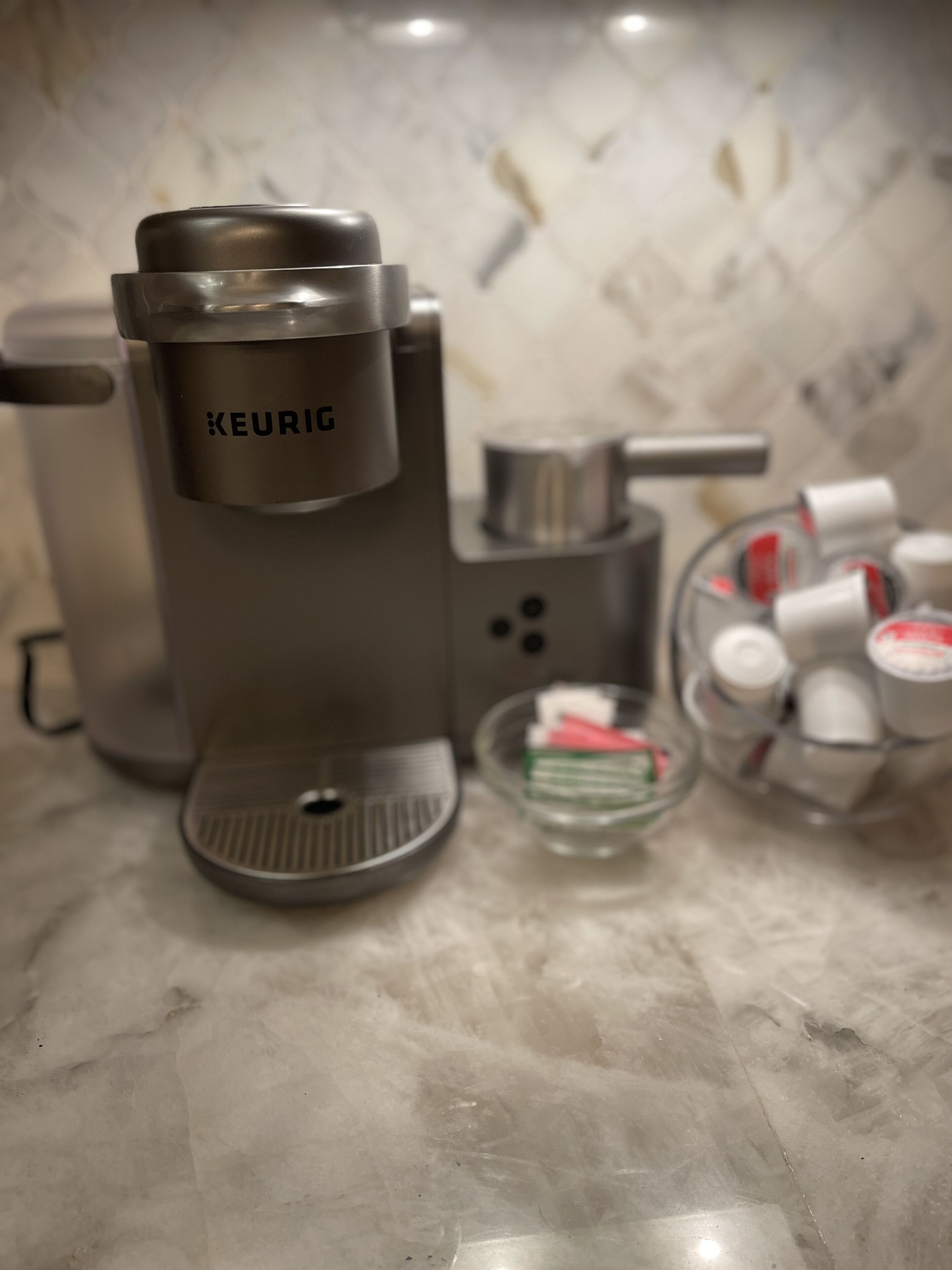 Een koffieapparaat met het label 'KEURIG' op een aanrecht met een marmeren achterwand.