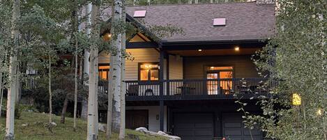 A two-story house with a covered driveway, surrounded by trees and a grassy area.
