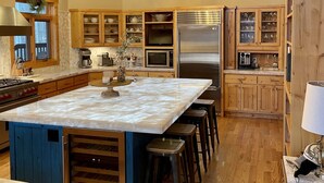 Une cuisine spacieuse dotée d’un grand îlot central, de meubles en bois, d’appareils électroménagers en acier inoxydable et d’un luminaire suspendu au design géométrique original.