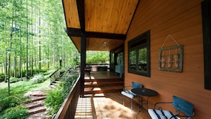 Une terrasse en bois avec un banc et une table, entourée d’une forêt.