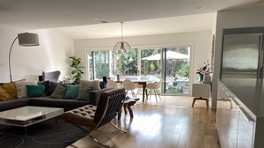 A modern living room with a sectional sofa, a coffee table, and a dining area with chairs and a table. - Ultimate Summer Vacation Home (Los Angeles)