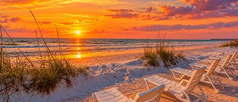 A beach with white lounge chairs and a sunset.