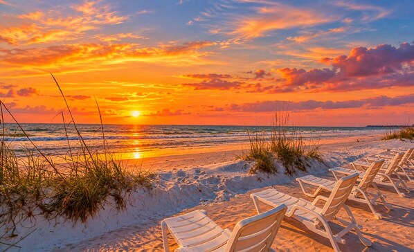 A beach with white lounge chairs and a sunset.