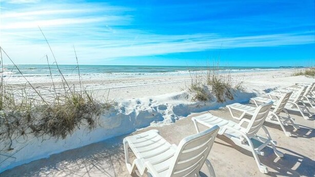 A beach with white lounge chairs and a clear blue sky.
