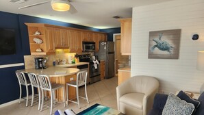 A modern kitchen with wooden cabinets, a central island with bar stools, a refrigerator, and a microwave.