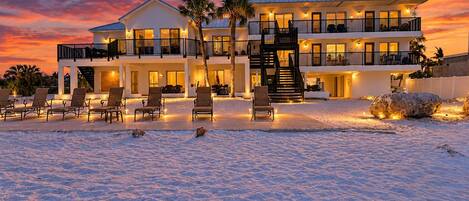 A beachfront property with a two-story building, outdoor seating, and a staircase leading to the upper level.