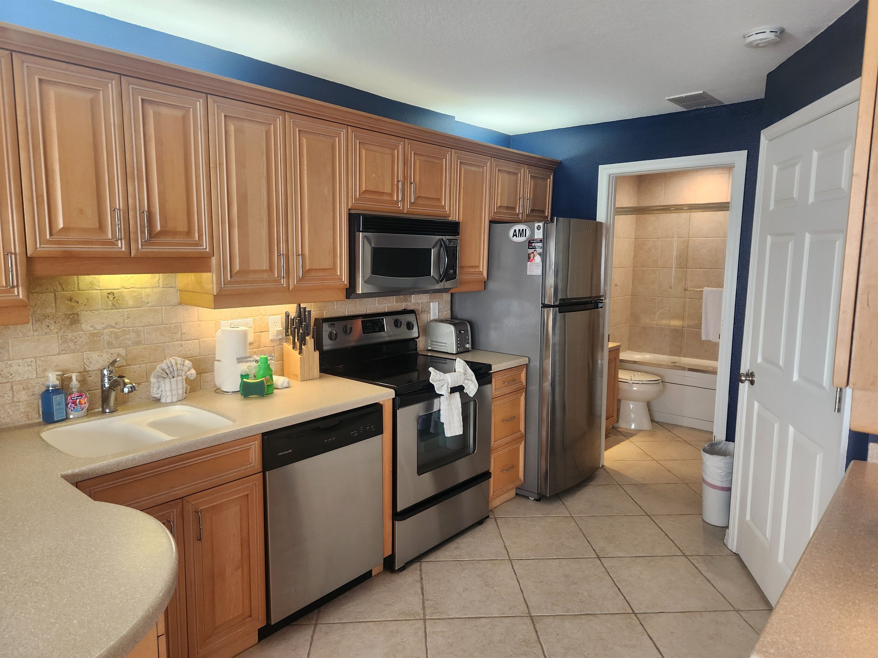 A kitchen with wooden cabinets, stainless steel appliances, a dishwasher, and a tiled floor.