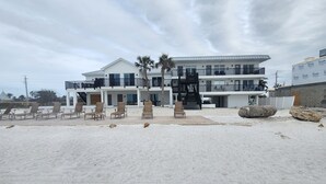 A beachfront hotel with multiple balconies, a pool area with lounge chairs, and a staircase leading to the upper floors.