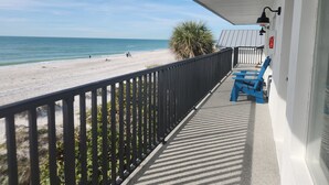 A balcony with a view of a beach and ocean. There are blue chairs and a fire extinguisher on the wall.