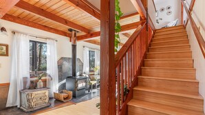 Una escalera de madera conduce a una sala de estar con chimenea, vigas de madera y vistas al exterior.