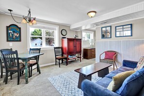 A living room with a dining area, a blue sofa, a wooden coffee table, a chandelier, and a framed picture of lighthouses.