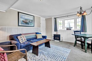 A living room with a blue sofa, a wooden coffee table, a wicker chair, a fireplace, and a dining table with chairs.