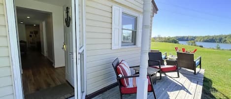 A wooden deck with outdoor furniture, a door leading inside, and a view of a lake.