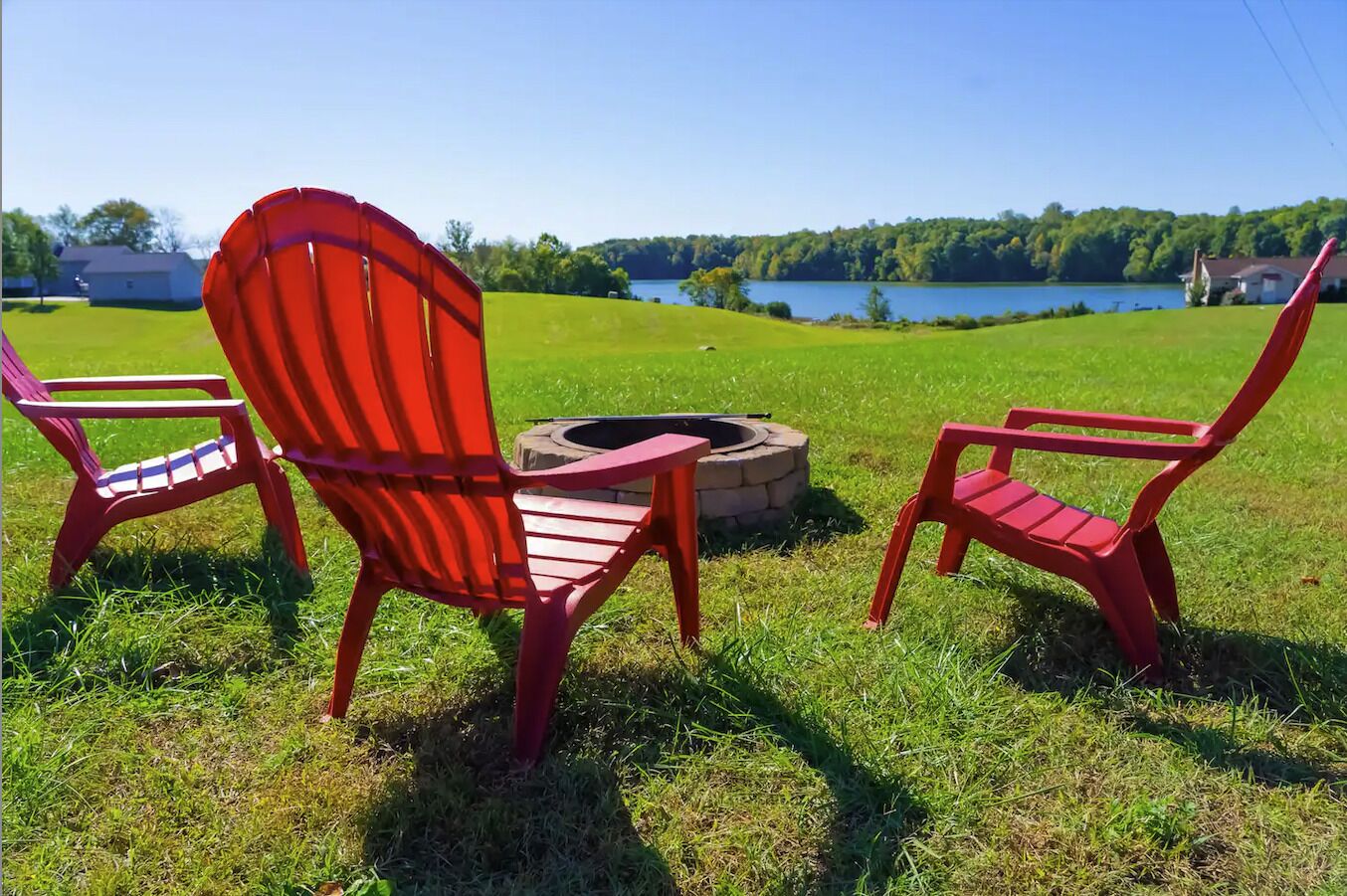 A grassy outdoor area with a fire pit and three red Adirondack chairs.
