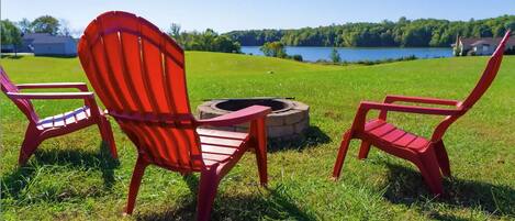 A grassy outdoor area with a fire pit and three red Adirondack chairs.