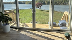 A room with a large sliding glass door leading to a deck with a view of a lake and forest. - Whippoorwill Cottage - Dock, Fire Pit, Boat Launch, Spectacular Views (Mineral)