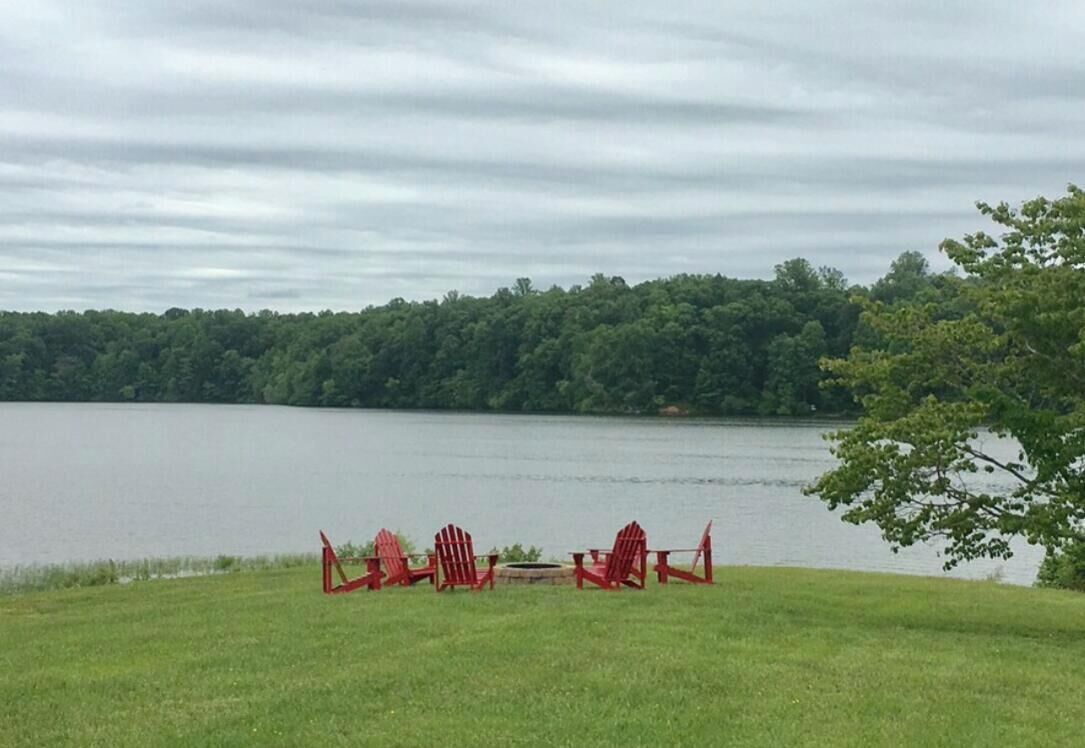 A lakeside view with a grassy area and red Adirondack chairs.