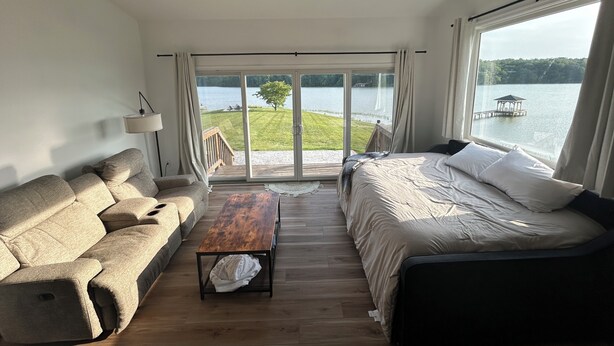 A bedroom with a bed, a sofa, a table, and a view of a lake and dock. - Whippoorwill Cottage - Dock, Fire Pit, Boat Launch, Spectacular Views (Mineral)