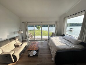 Un dormitorio con cama, sofá, mesa y vista a un lago y un muelle.
