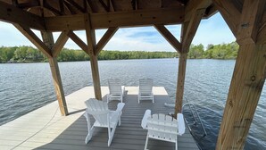 A wooden deck with white Adirondack chairs and a small table, overlooking a calm lake. - Whippoorwill Cottage - Dock, Fire Pit, Boat Launch, Spectacular Views (Mineral)