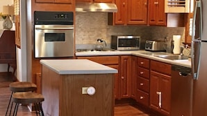 A kitchen with wooden cabinets, stainless steel appliances, and a central island with stools. - Whippoorwill Cottage - Dock, Fire Pit, Boat Launch, Spectacular Views (Mineral)