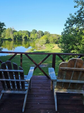 Une terrasse en bois avec des fauteuils Adirondack donnant sur un lac et une végétation luxuriante.