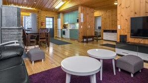A log cabin interior with a dining area, kitchen, living room, and a TV.