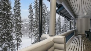 A snow-covered balcony with a view of snow-laden trees and a clear sky.