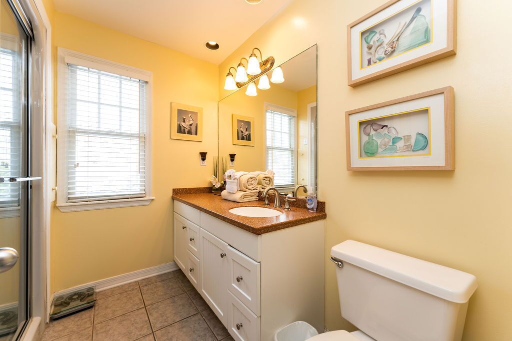 A bathroom with a sink, toilet, and a shower area. There are framed pictures on the wall and a towel rack with towels.