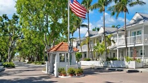A hotel with a white facade, a red-tiled roof, and a flagpole with an American flag. - Roosters Perch at Truman Annex- LOW SUMMER RATES!!! (Key West)