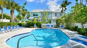 Relax by the clear blue pool surrounded by lush greenery and lounge chairs.