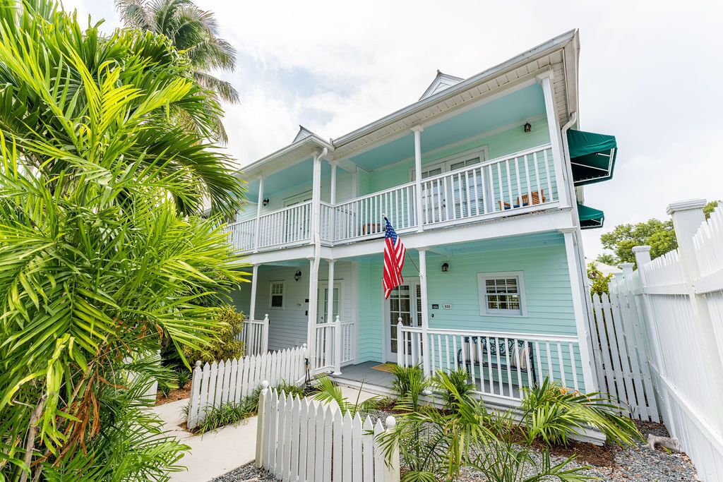 A two-story house with a porch, a flag, and a white picket fence.