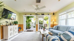 A living room with a ceiling fan, a television, a sofa, and a dining area. - Roosters Perch at Truman Annex- LOW SUMMER RATES!!! (Key West)