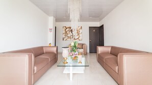 Una sala de estar moderna con una mesa de centro de vidrio, dos sofás de cuero, una araña y un cuadro grande con motivos florales en la pared.