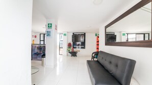 Un área de espera moderna con un sofá de cuero negro, una mesa de vidrio y un espejo grande.