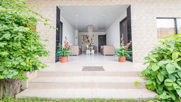 Una entrada moderna con un muro de ladrillo, una escalera que conduce a una sala de estar con sofás y una mesa de centro, y plantas en macetas a cada lado.