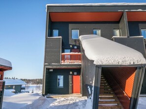 A multi-story building with a red door, a balcony with railings, and a staircase leading to an upper level. - Skivillas 61 ukkohalla (b1) by Interhome (Hyrynsalmi)